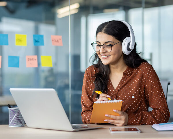 Woman with headphones taking notes at laptop